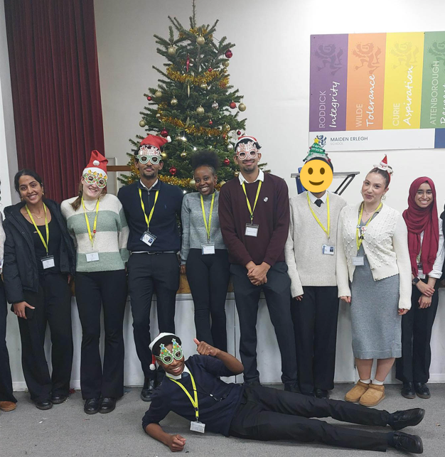 A picture of 9 Sixth Form students in posed with various Christmas items in front of a decorated Christmas Tree.